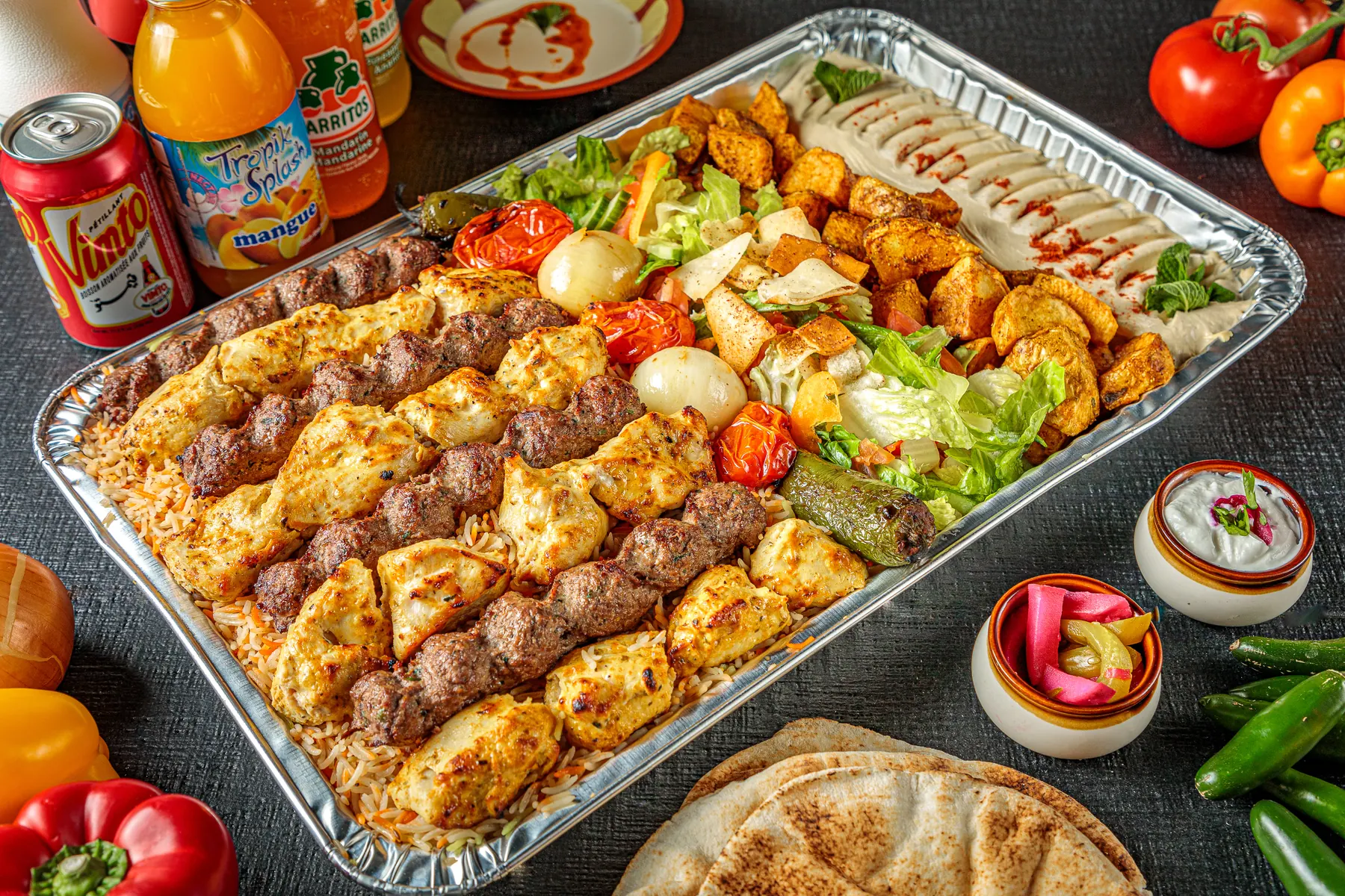 A catering tray of kebabs and shish tawouk with pita, vegetables and dips