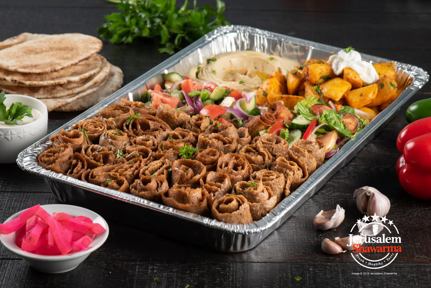 A tray of beef shawarma with pita, pickles and garlic sauce